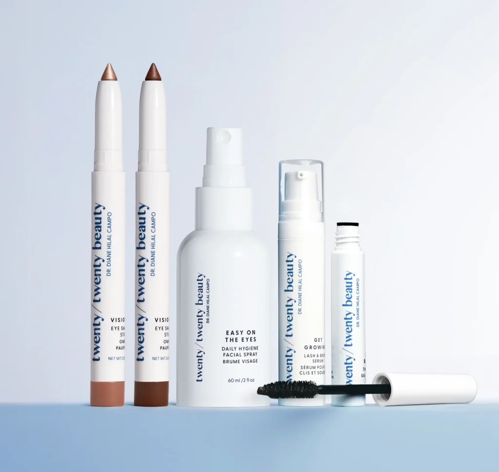 wenty/Twenty Beauty eye makeup and skincare products including eyeshadow sticks, a daily perfecting spray, a lash and brow serum, and mascara, arranged on a light stone block against a clean white background.
